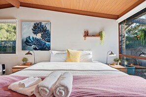 Una camera da letto con un letto, cuscini, un quadro, comodini con lampade e una finestra vista.