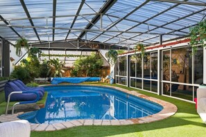 A covered swimming pool with a glass enclosure, surrounded by artificial grass and seating. - Rural Getaway: Alpacas, Pool, Hot tub, Gym, Tennis (Sandford)