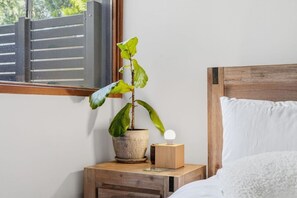 A bedside table with a potted plant, a wooden nightstand, a lamp, and a bed with a white pillow. - Rural Getaway: Alpacas, Pool, Hot tub, Gym, Tennis (Sandford)