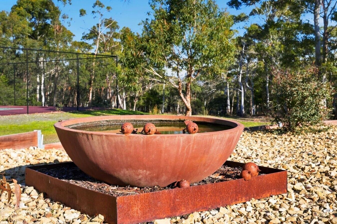 A circular outdoor fire pit with four spherical decorations, surrounded by a metal frame and set on a bed of wood chips.