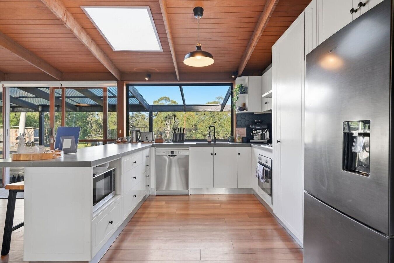 A modern kitchen with a central island, stainless steel appliances, and a large window overlooking a garden.