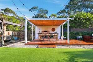 En udendørs terrasse med et træbeklædt pergola, grill og siddepladser.
