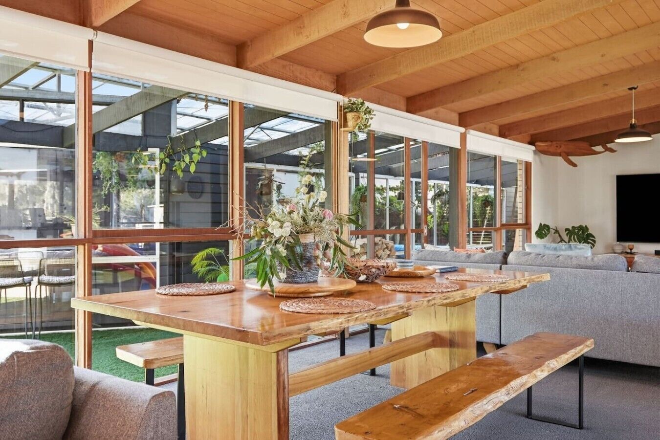 A spacious living area with a wooden dining table, benches, and a grey sofa.