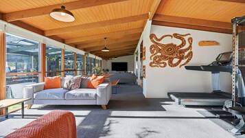 A modern living room with a grey sofa, orange cushions, a treadmill, and a large window.