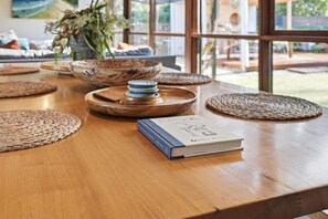 A wooden table with woven placemats, a book, and a stack of blue plates. - Rural Getaway: Alpacas, Pool, Hot tub, Gym, Tennis (Sandford)