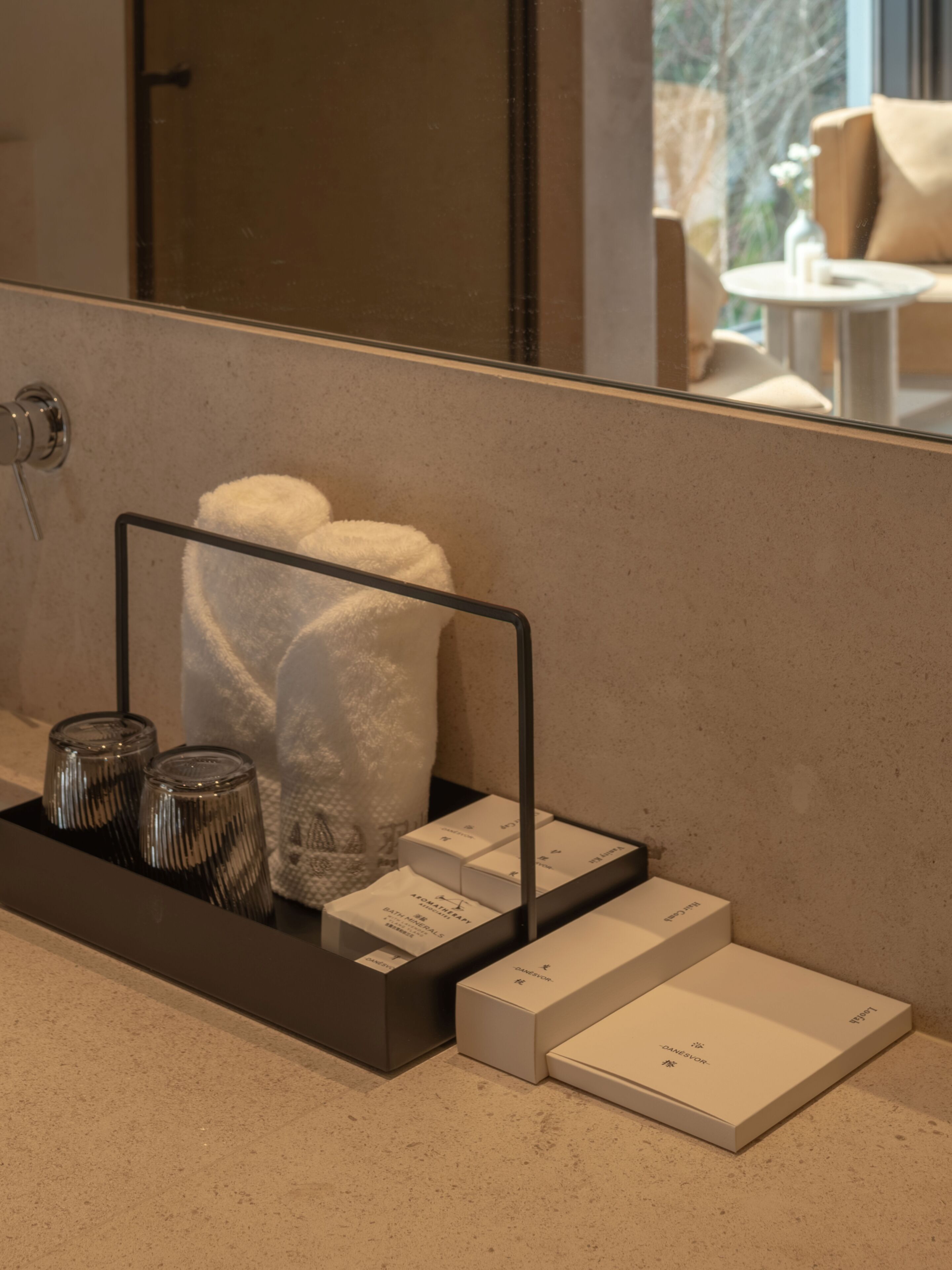 A bathroom vanity with a towel rack holding two towels, a glass candle holder, and a set of toiletries.