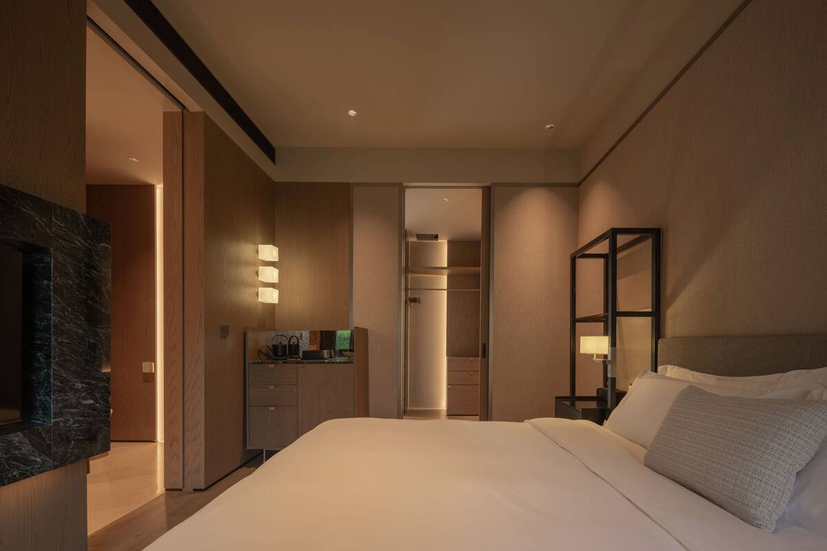 Una habitación de hotel moderna con una cama grande, televisor incorporado, un escritorio con computadora y un vestidor.