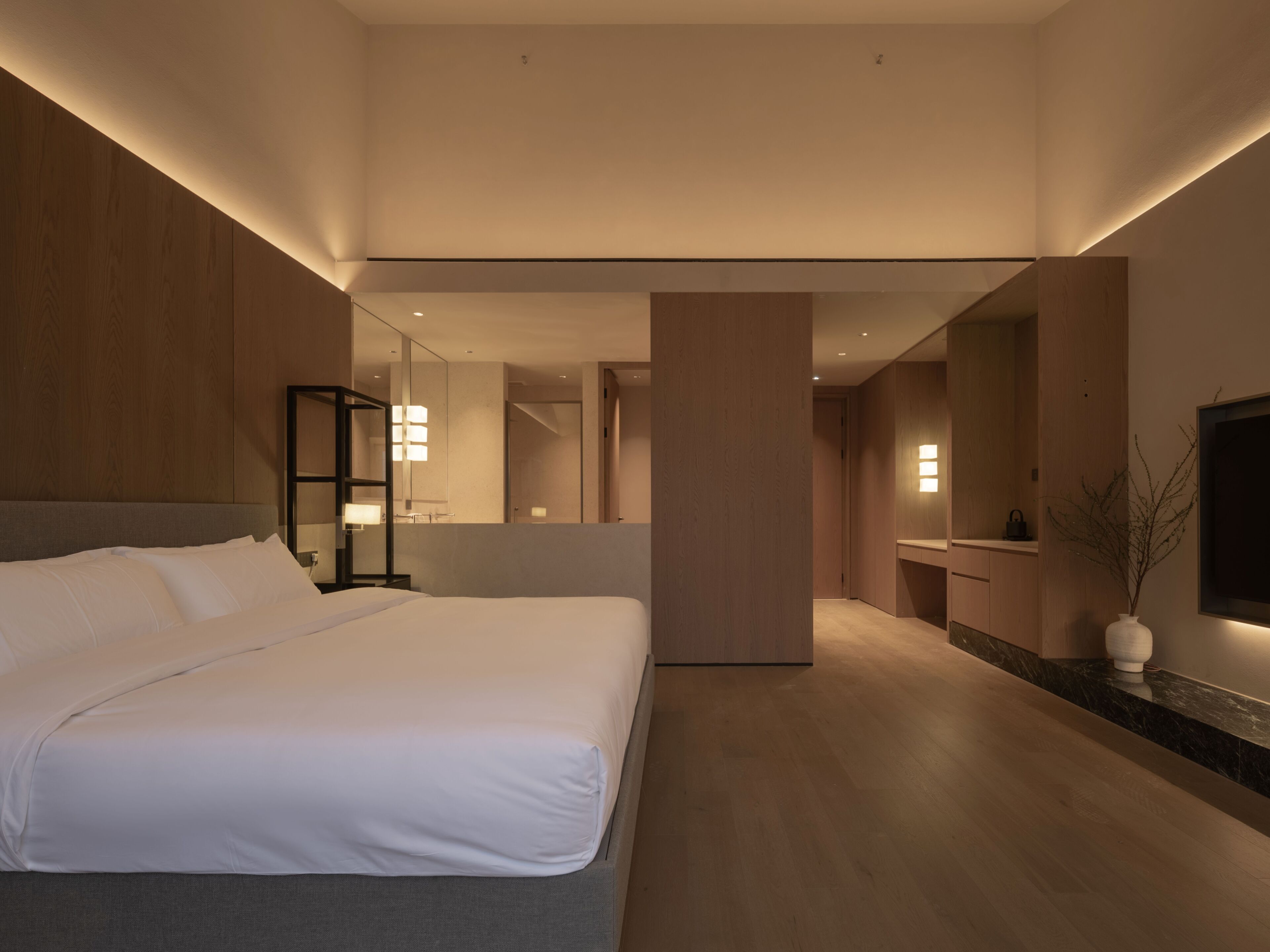 A modern hotel room with a large bed, a mirror, a vanity, and a TV.