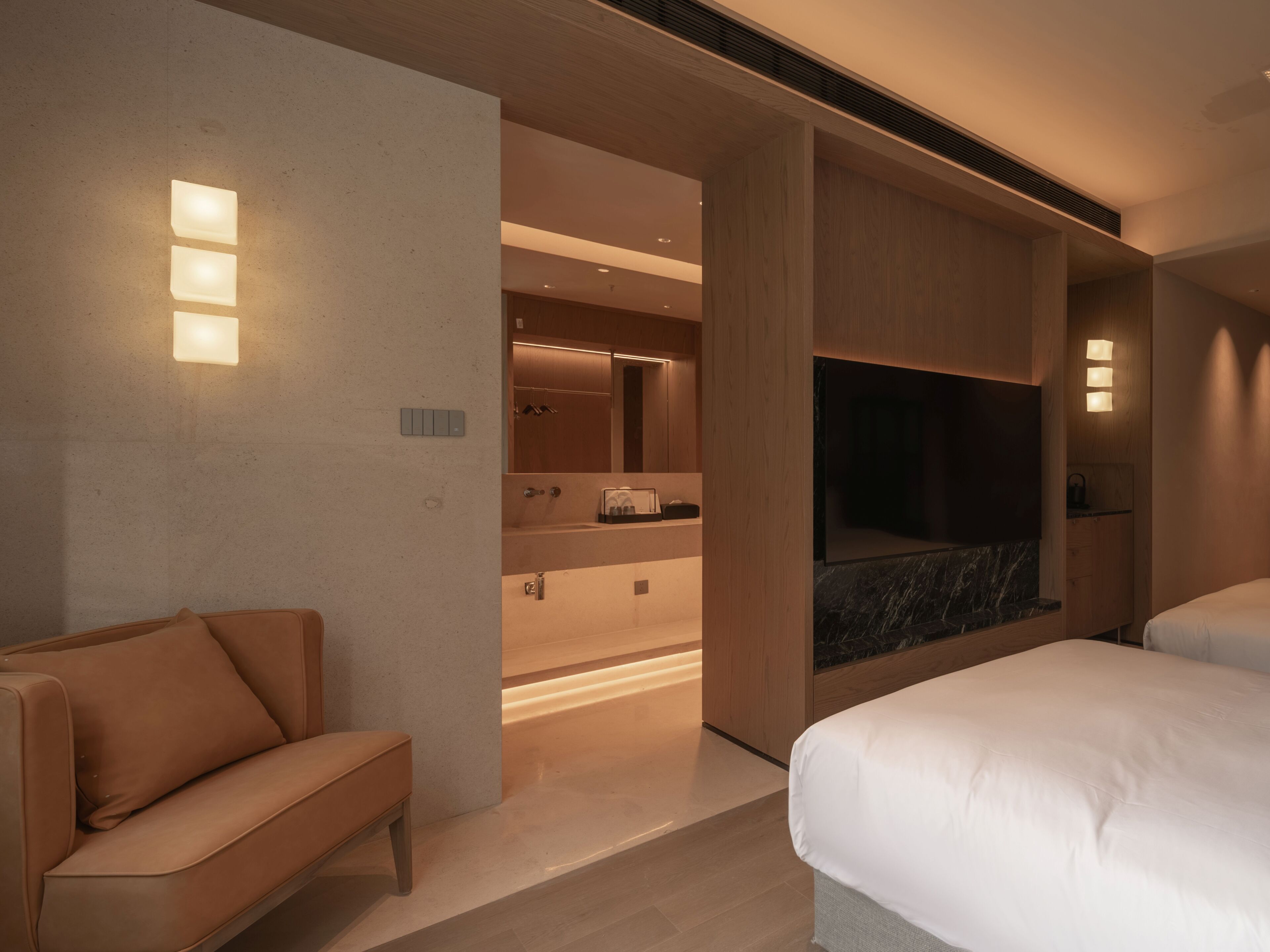 A modern hotel room with a sofa, a bed, a TV, and a bathroom with a mirror and sink.