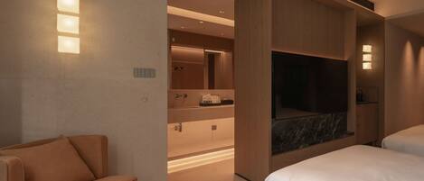 A modern hotel room with a sofa, a bed, a TV, and a bathroom with a mirror and sink.