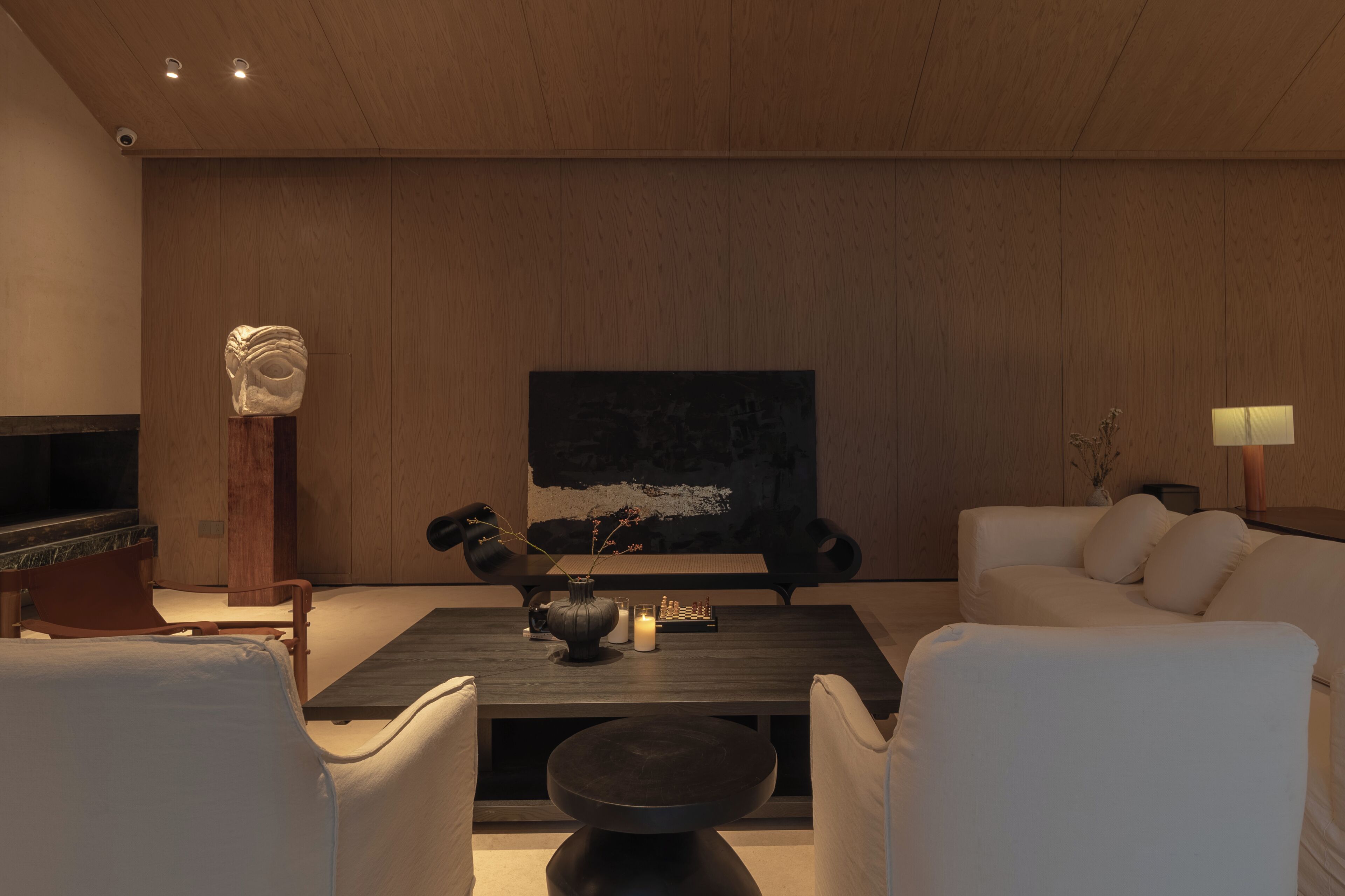 A modern living room with a dark wooden coffee table, white sofas, a stone sculpture, and a painting on the wall.