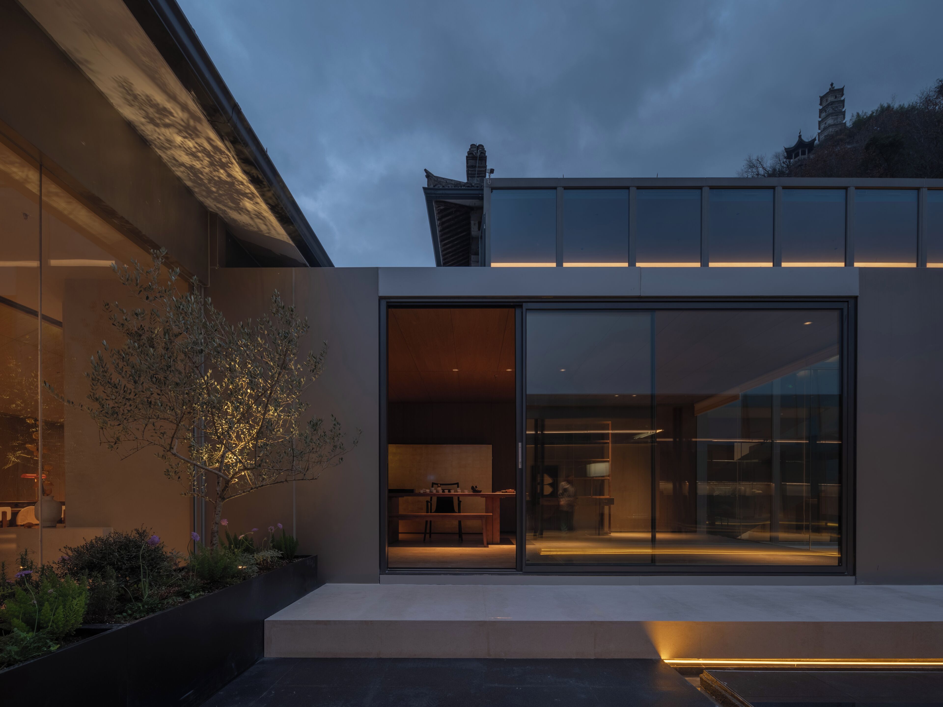 A modern building with large glass windows, a flat roof, and a tree in the foreground.