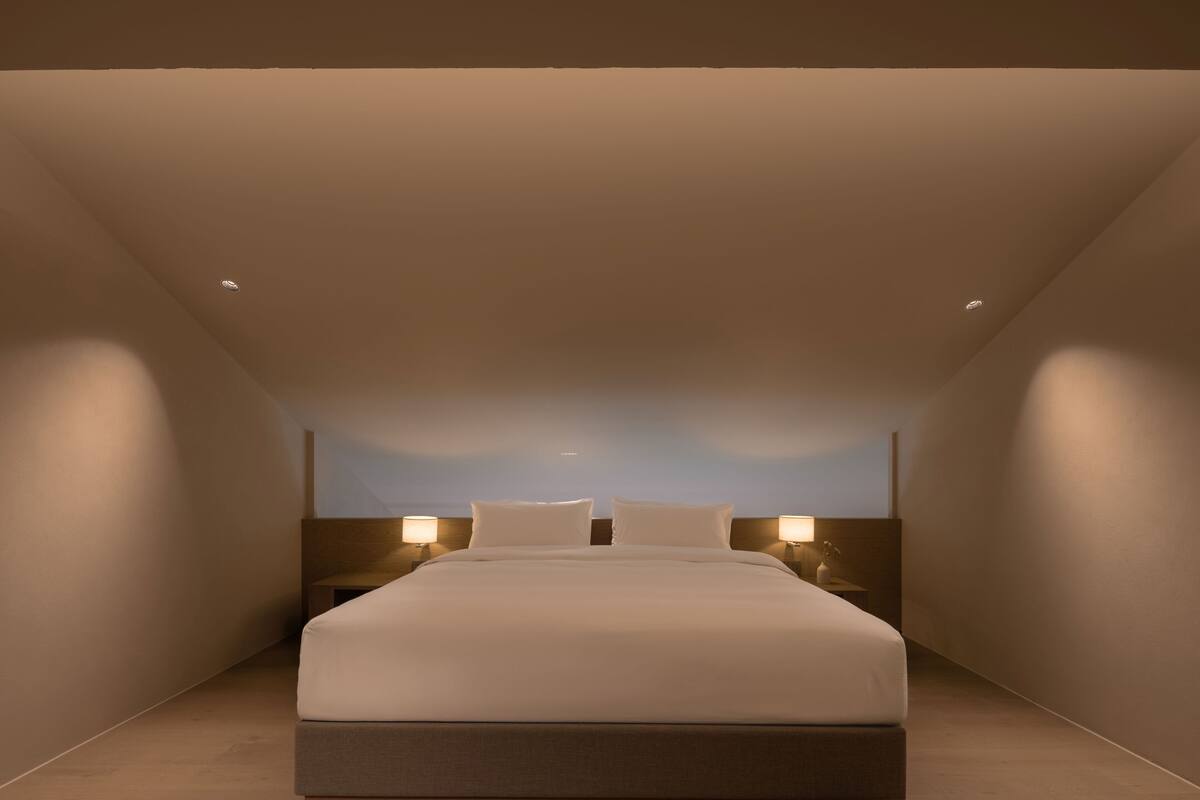 Una habitación de hotel moderna con una cama grande, lámparas de noche y un techo inclinado.