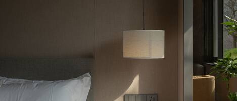Ein modernes Hotelzimmer mit Bett, Nachttisch, Lampe, Steckdose und einer Zimmerpflanze.