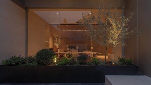 A modern building with a glass facade, a tree in the foreground, and a bench area with plants. - Hayama Pagoda Villa (Taizhou)