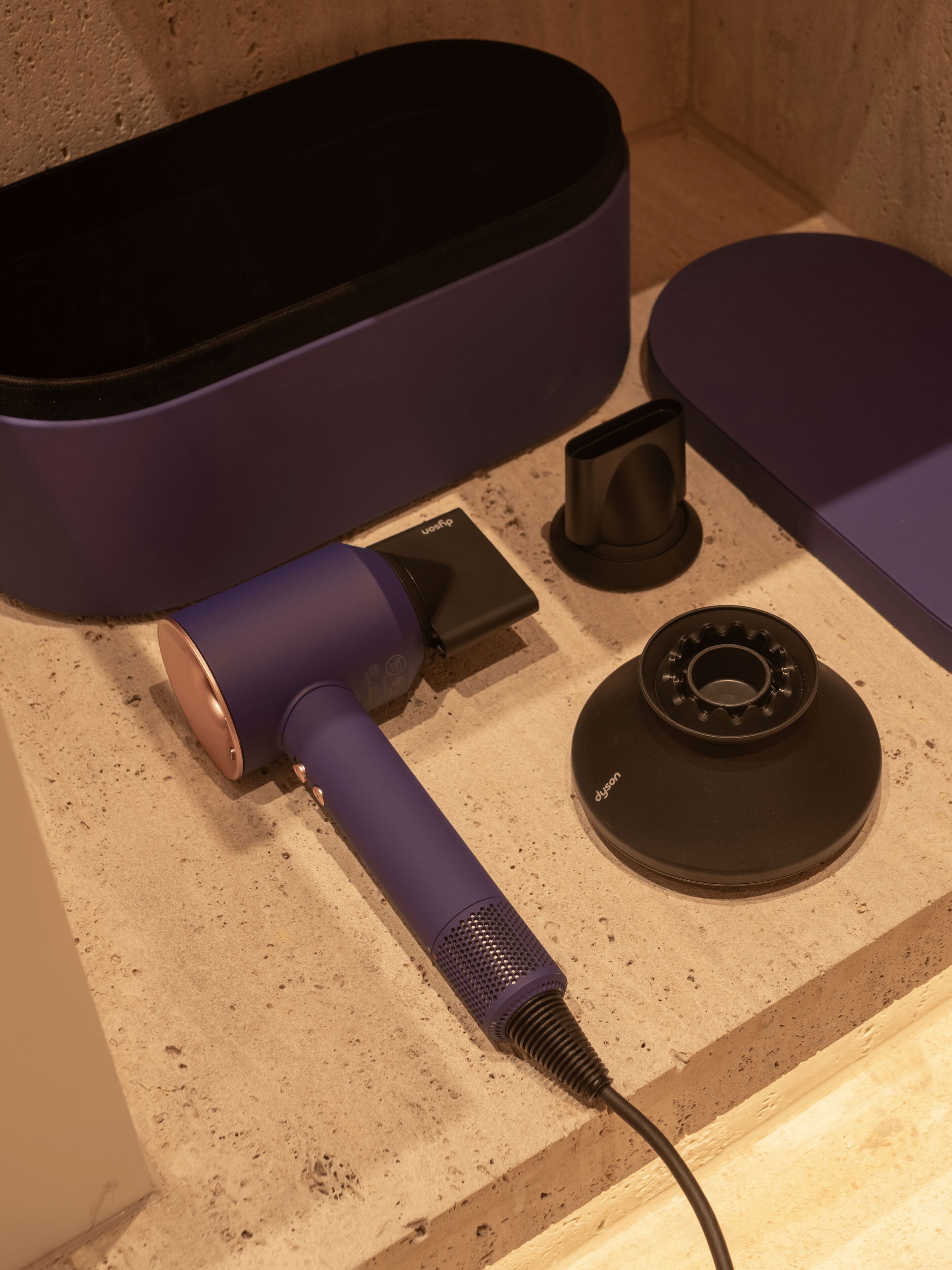 Un secador morado, una base de carga negra y un dispositivo circular negro sobre una encimera.