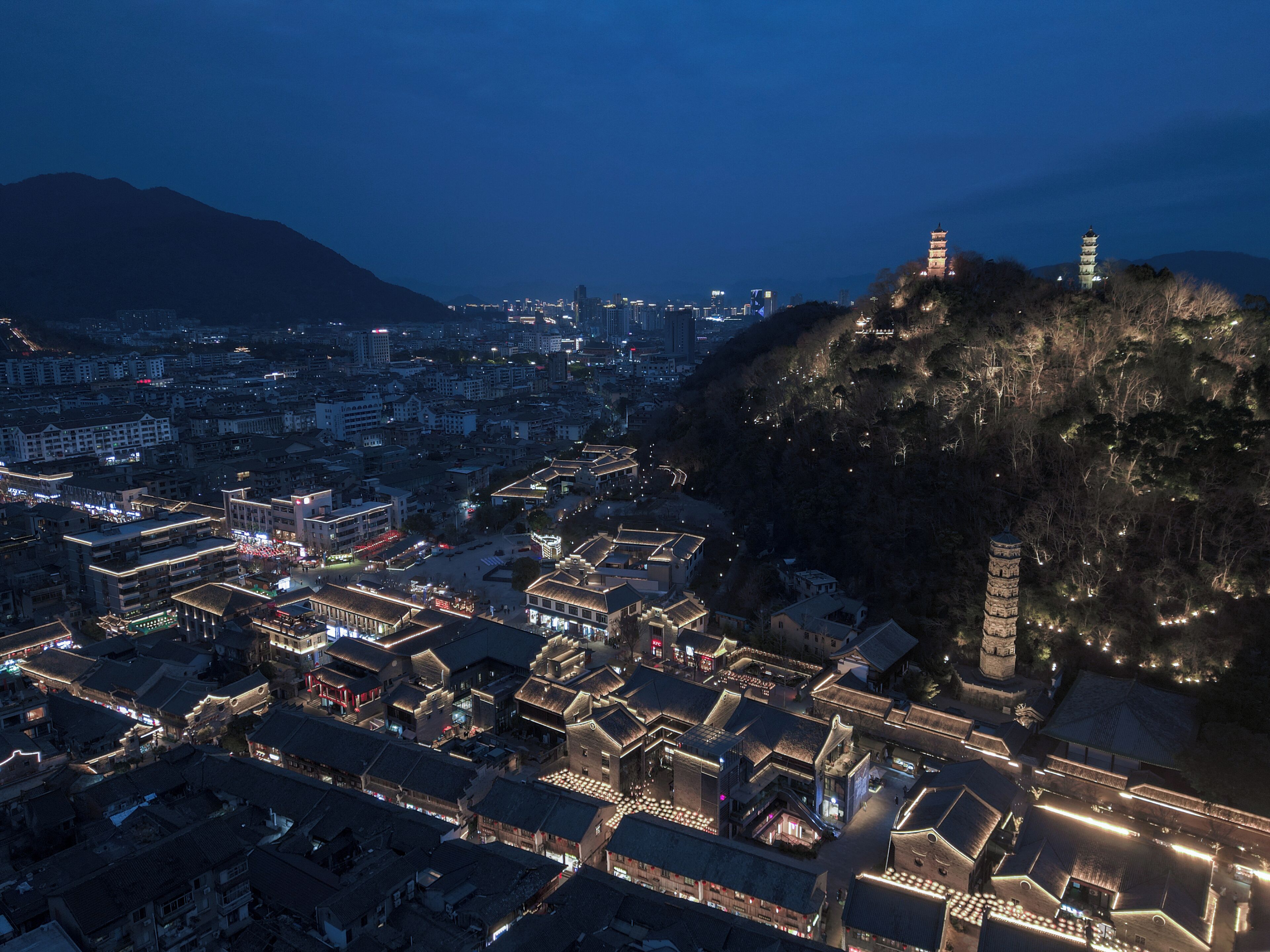 A traditional village with tiered pagoda-style buildings, a central open square, and a mountain backdrop.