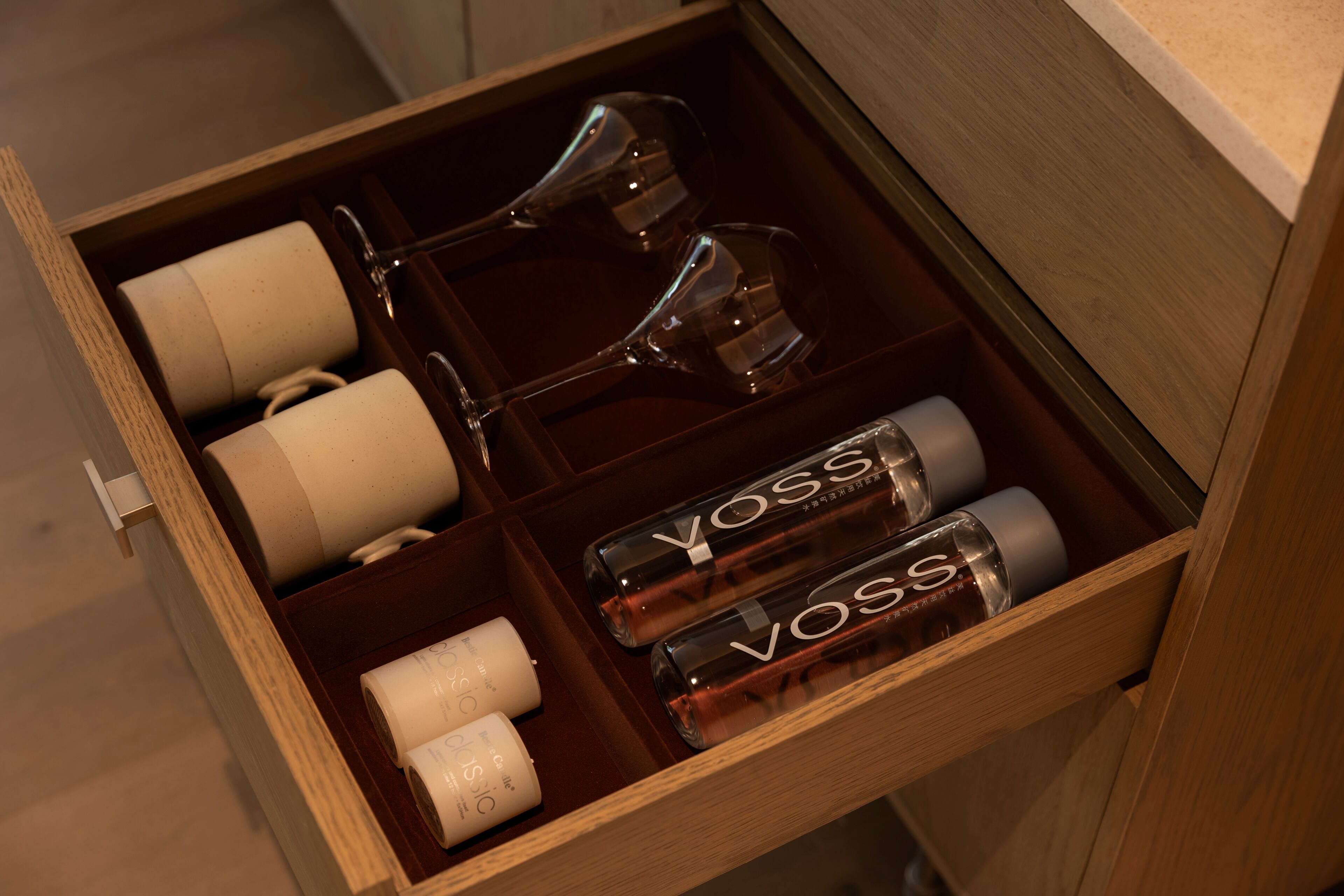 Un cajón con copas de vino, corchos y botellas con la etiqueta 'VOSS'.