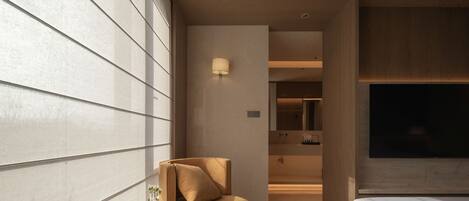 A modern hotel room with a sofa, a small round table with a vase, a bed, and a TV.