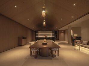 A modern hotel room with a large wooden dining table, a built-in kitchen, and a cozy seating area. - Hayama Pagoda Villa (Taizhou)