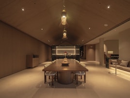 Una habitación de hotel moderna con una amplia mesa de comedor de madera, una cocina integrada y una zona de estar acogedora.
