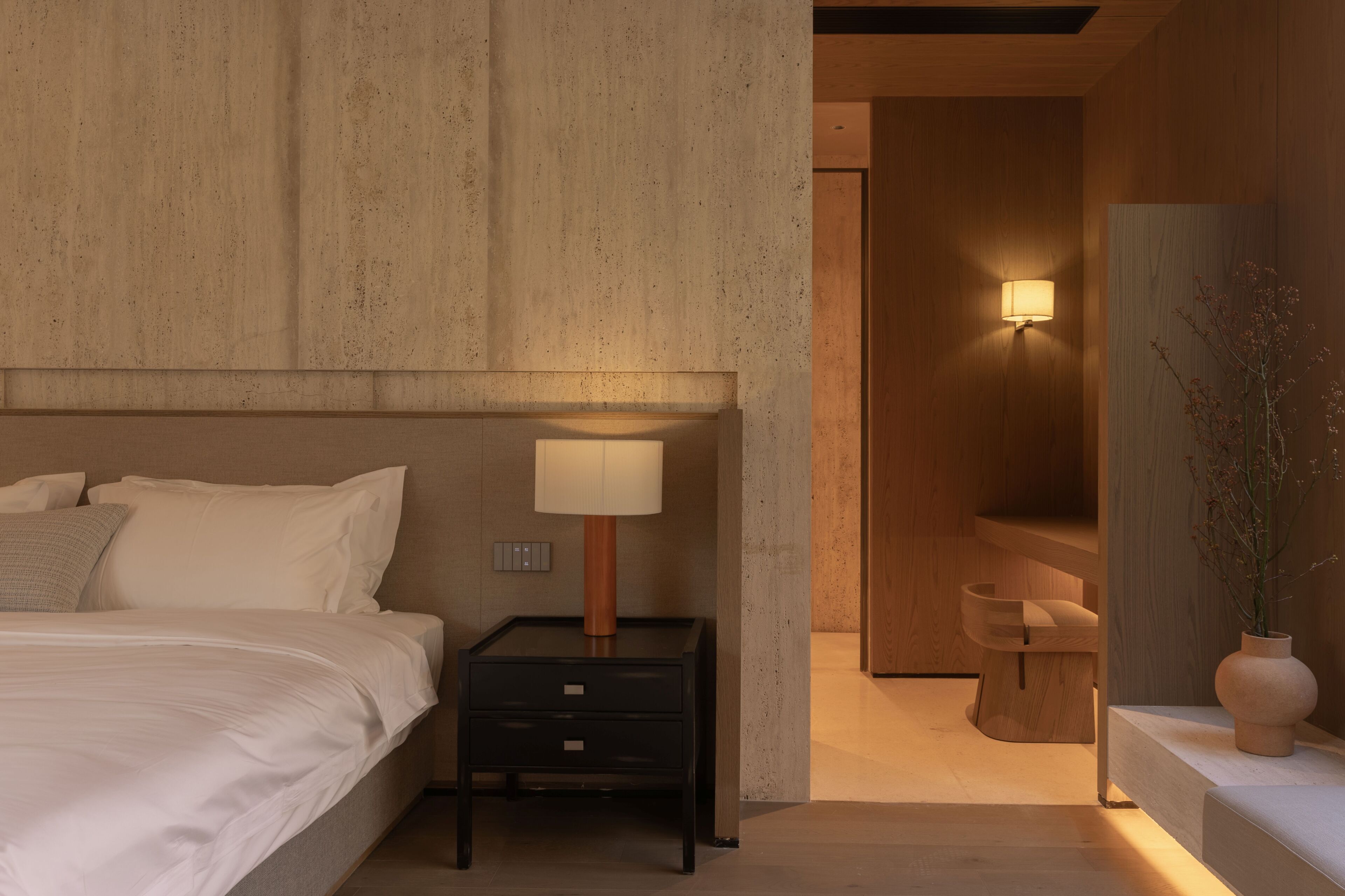 A bedroom with a bed, bedside table, lamp, and a wooden bench.