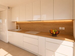 A modern kitchen with white cabinetry, a wooden countertop, a sink, and a fruit bowl. - Exceptional Seafront Apartment • 180° Sea View • Walk to Beach • D-Day Beaches (Colleville-Montgomery)