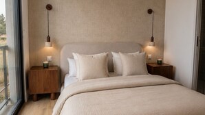 Une chambre à coucher avec un grand lit, deux tables de chevet, une lampe fixée au mur et une fenêtre.