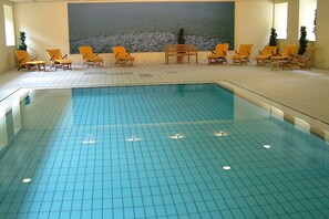 An indoor swimming pool with tiled flooring, surrounded by orange lounge chairs and a mural of a rocky landscape. - Relaxing Superior Double Room | Perfect for Couples & Getaways (Köln)