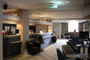 A hotel lobby with a reception desk, seating area, and a stone wall. - Relaxing Superior Double Room | Perfect for Couples & Getaways (Köln)