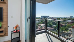 Un balcón con vista a la ciudad, una pequeña mesa con un florero y un televisor de pared.