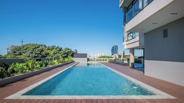 Una piscina en la azotea con vistas despejadas del horizonte urbano, rodeada de edificios modernos y vegetación.