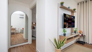Una sala de estar moderna con una televisión de pantalla plana, estanterías de madera, un espejo y una planta en maceta.