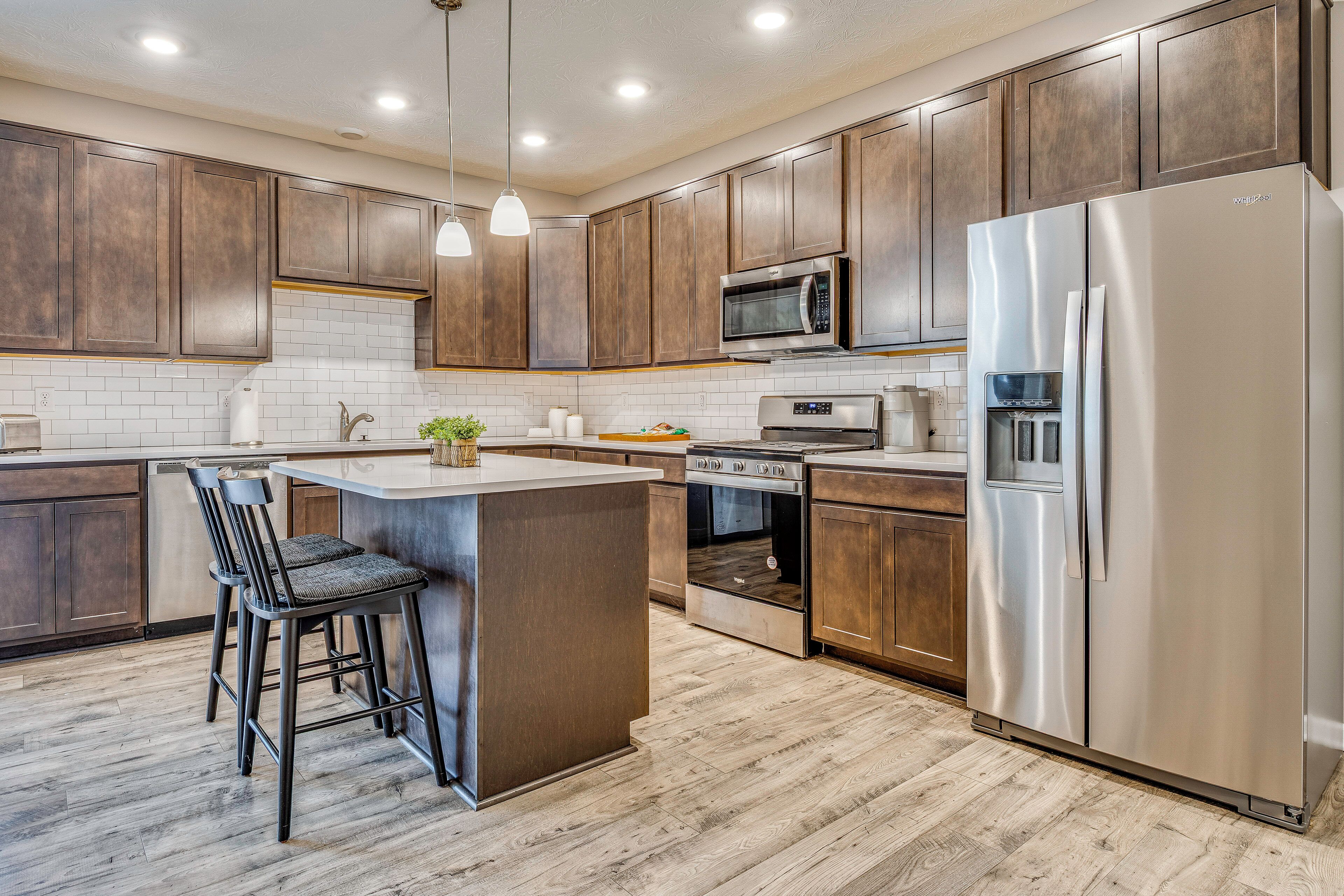 A modern kitchen with wooden cabinets, stainless steel appliances, and a central island with bar stools.