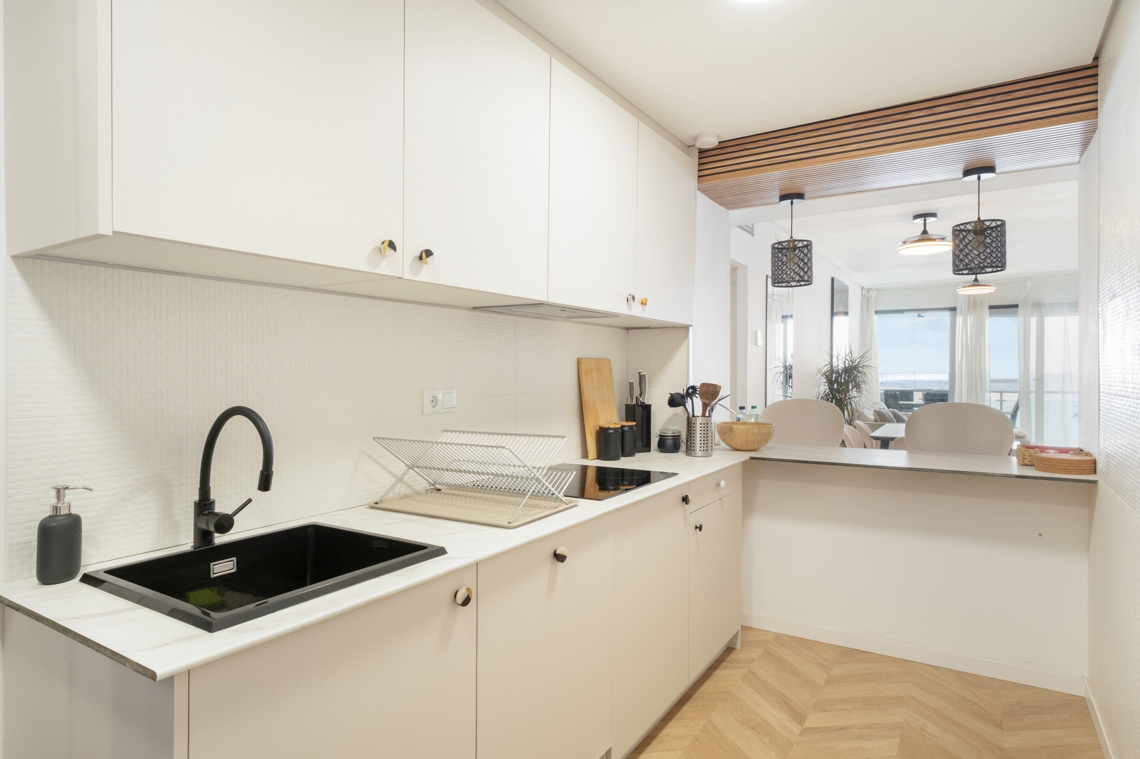 Una cocina moderna con armarios blancos, un lavamanos negro y una encimera de madera.
