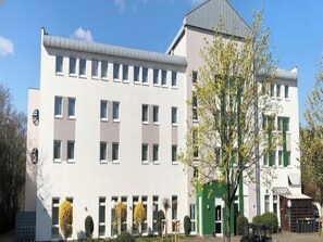 Ein mehrstöckiges Gebäude mit flacher Fassade, zahlreichen Fenstern und einem grünen Eingang.