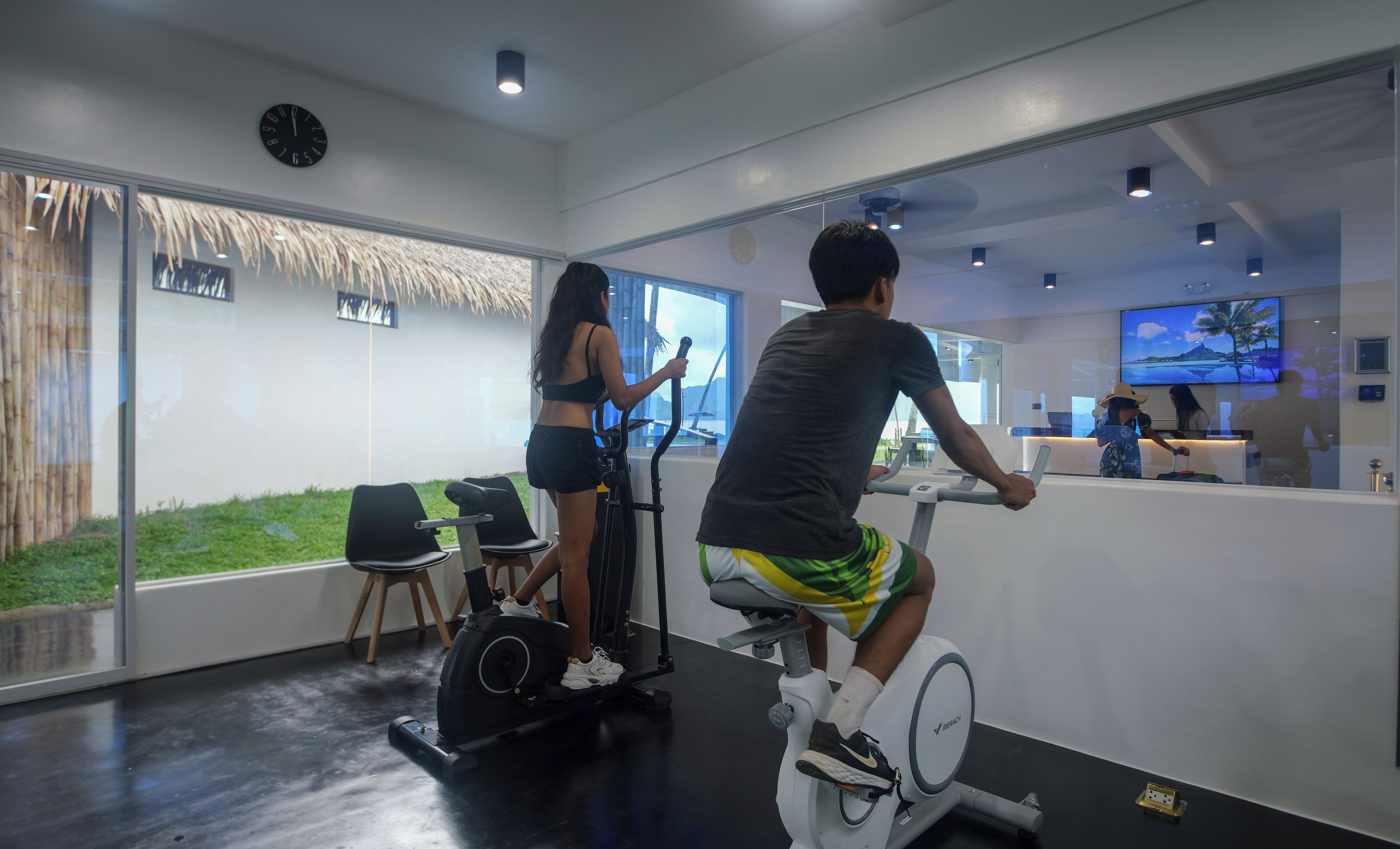 A gym with stationary bikes, a reception desk, and a large window with a view of the outdoors.