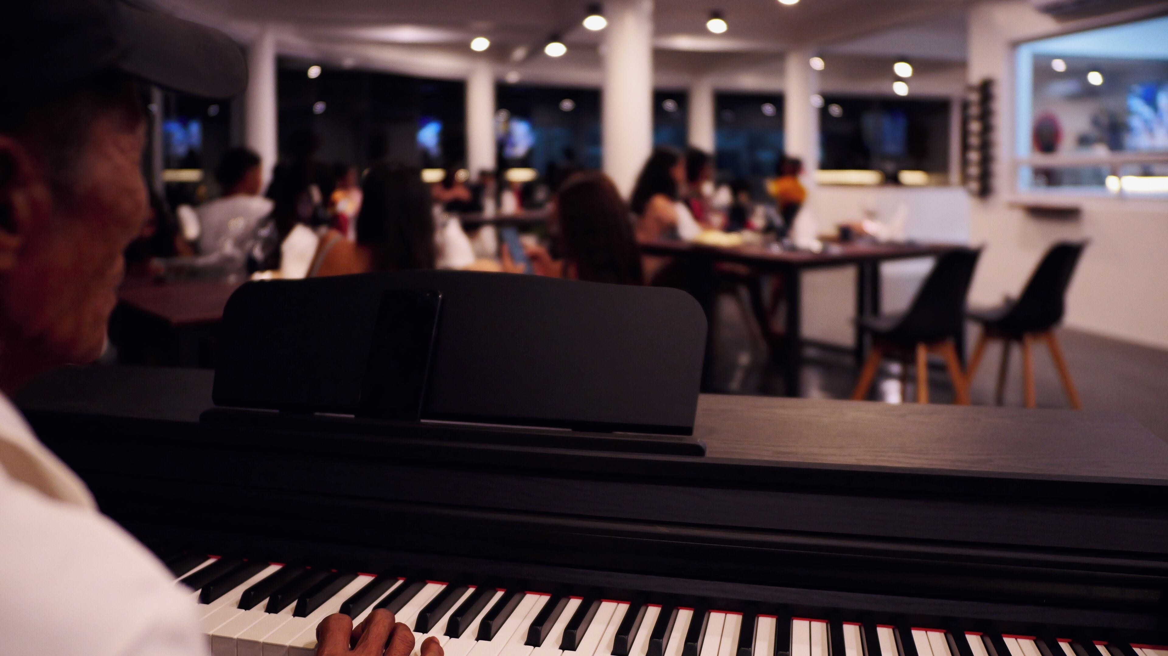 Un piano en un ambiente interior moderno, con personas en el fondo.
