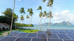 Solar panels, palm trees, a pool, and a view of the sea and mountains.