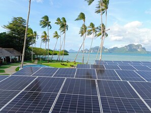 Solar panels, palm trees, a pool, and a view of the sea and mountains. - Bebeladan Beach Resort (El Nido)