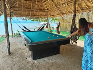 A pool table with balls, a person playing, and a view of the sea.