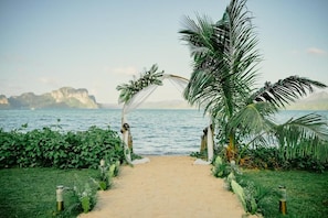 A pathway leading to a beach with a palm tree archway and a view of the sea and a distant island.