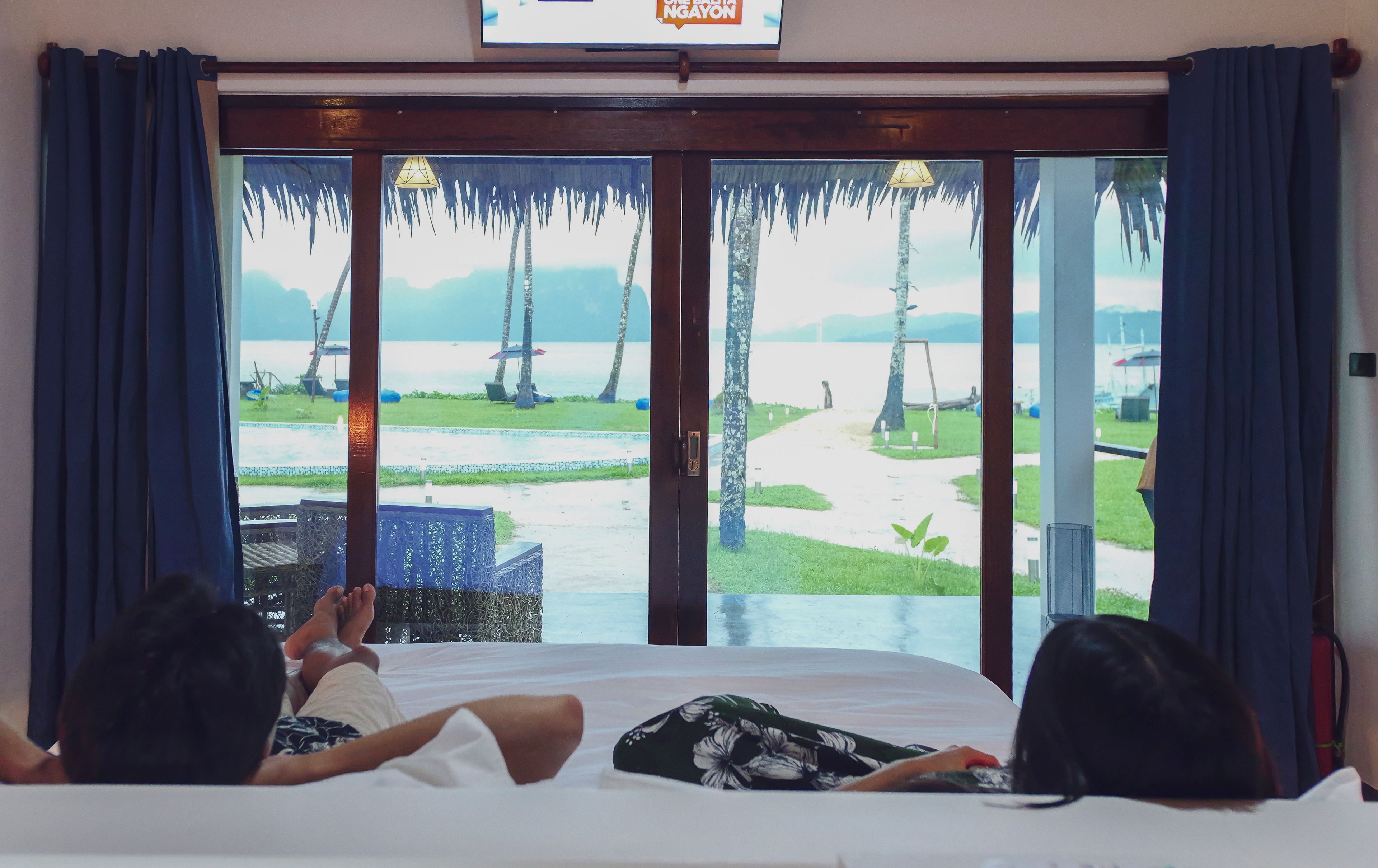 A room with a bed, a view of a beach, and a sign above the window.