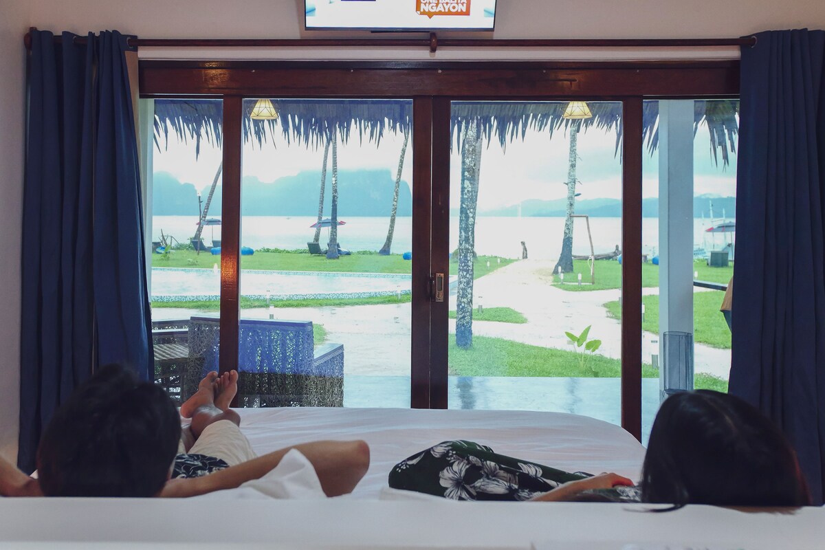 A room with a bed, a view of a beach, and a sign above the window.