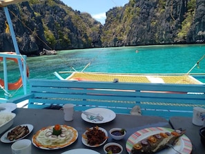 A dining table with various dishes and a view of a coastal area with clear turquoise water and rocky cliffs.