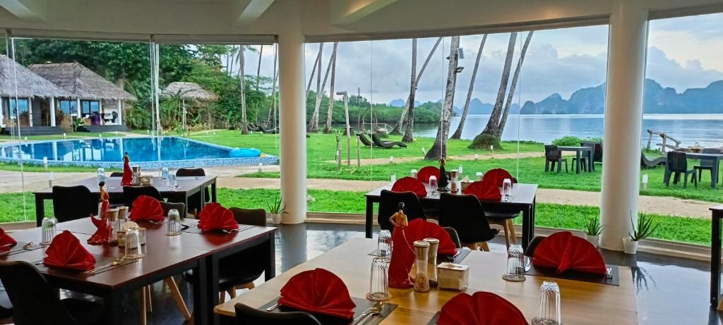 Un área de comedor al aire libre con mesas dispuestas para dos, con vista a una piscina y al agua.