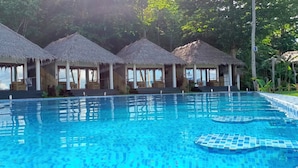 A pool with clear blue water, surrounded by thatched-roof structures.