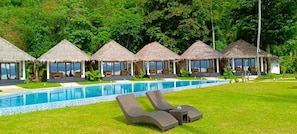 Un área junto a la piscina con estructuras de techo de paja y sillones de descanso.