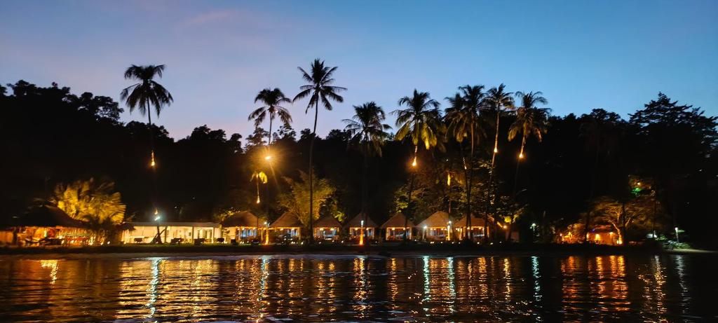 A waterfront property with overwater bungalows, palm trees, and a calm body of water reflecting lights.