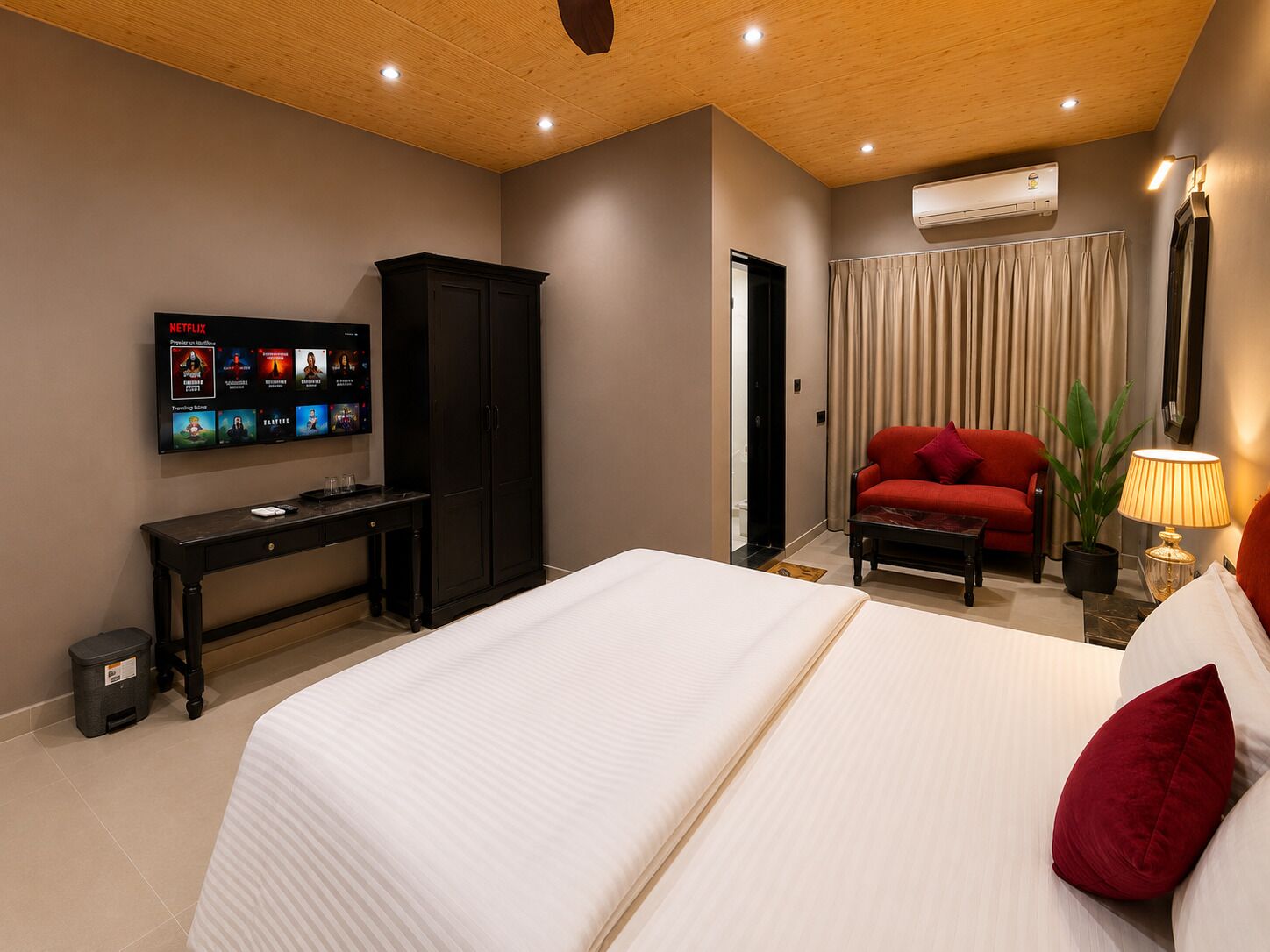 Habitación de hotel con cama, televisión, escritorio, armario, sofá rojo, lámpara y aire acondicionado.